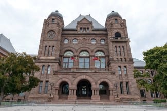 Toronto, Ontario, Canada Queens Park Romanesque facade of the Legislative Assembly of Ontario building and the Canadian flags flying .