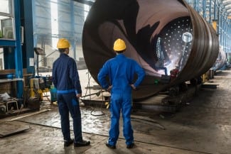 Two experienced workers supervising the manufacture of a metallic cylinder in the interior of a factory